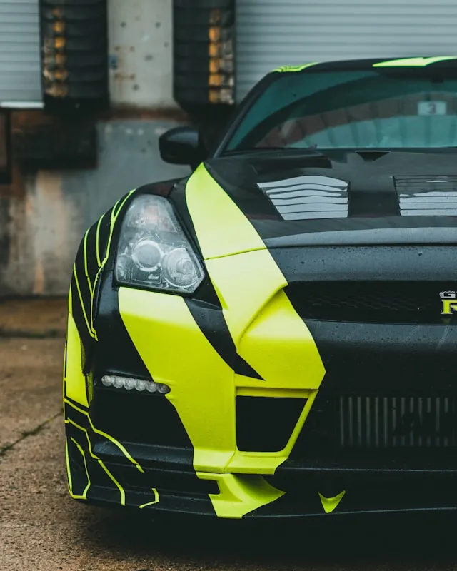 Black sports car with neon yellow camo-style vinyl wrap graphics on the front bumper and hood
